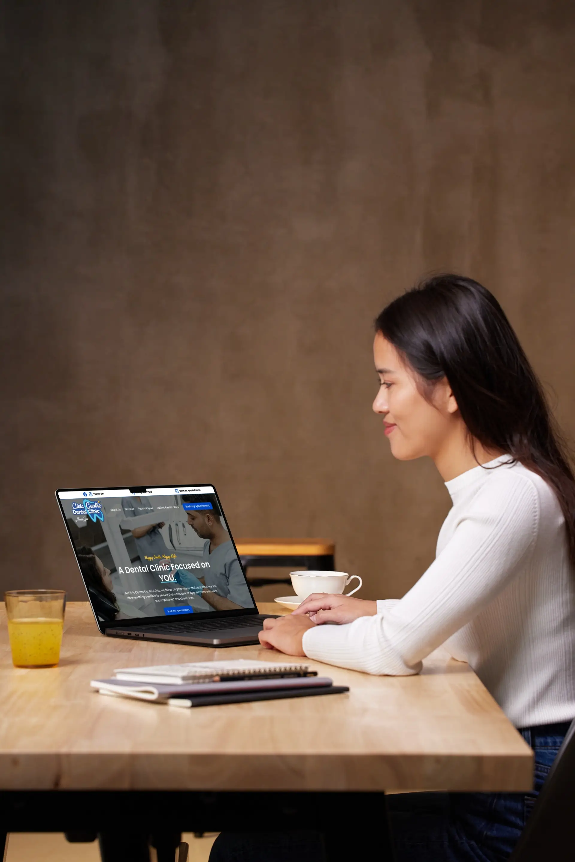 Woman sitting down in a well lit environnement, looking at the civic centre dental clinic website on her laptop.