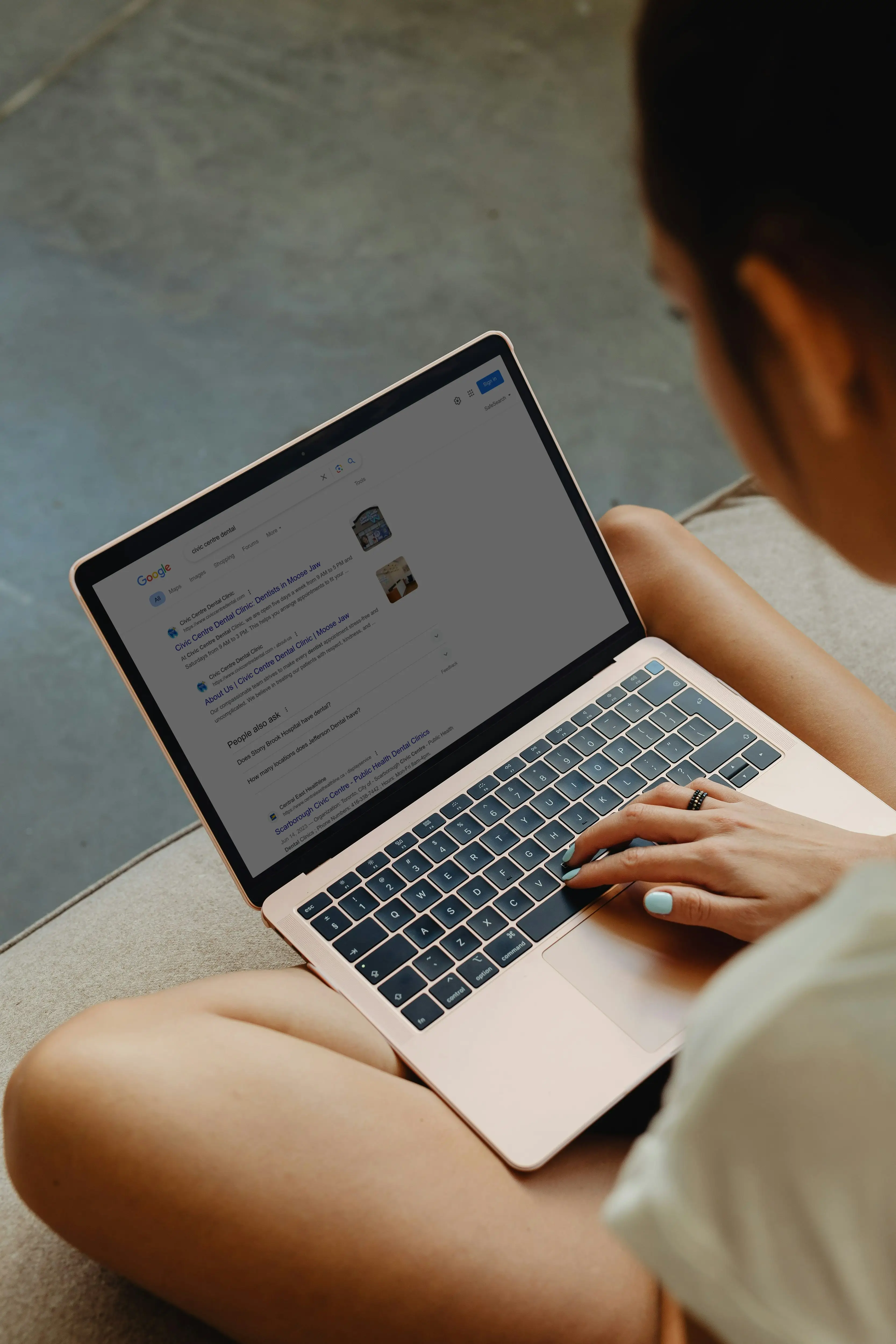Image of woman with laptop on her lap, looking at google search results for the term civic centre dental clinic.